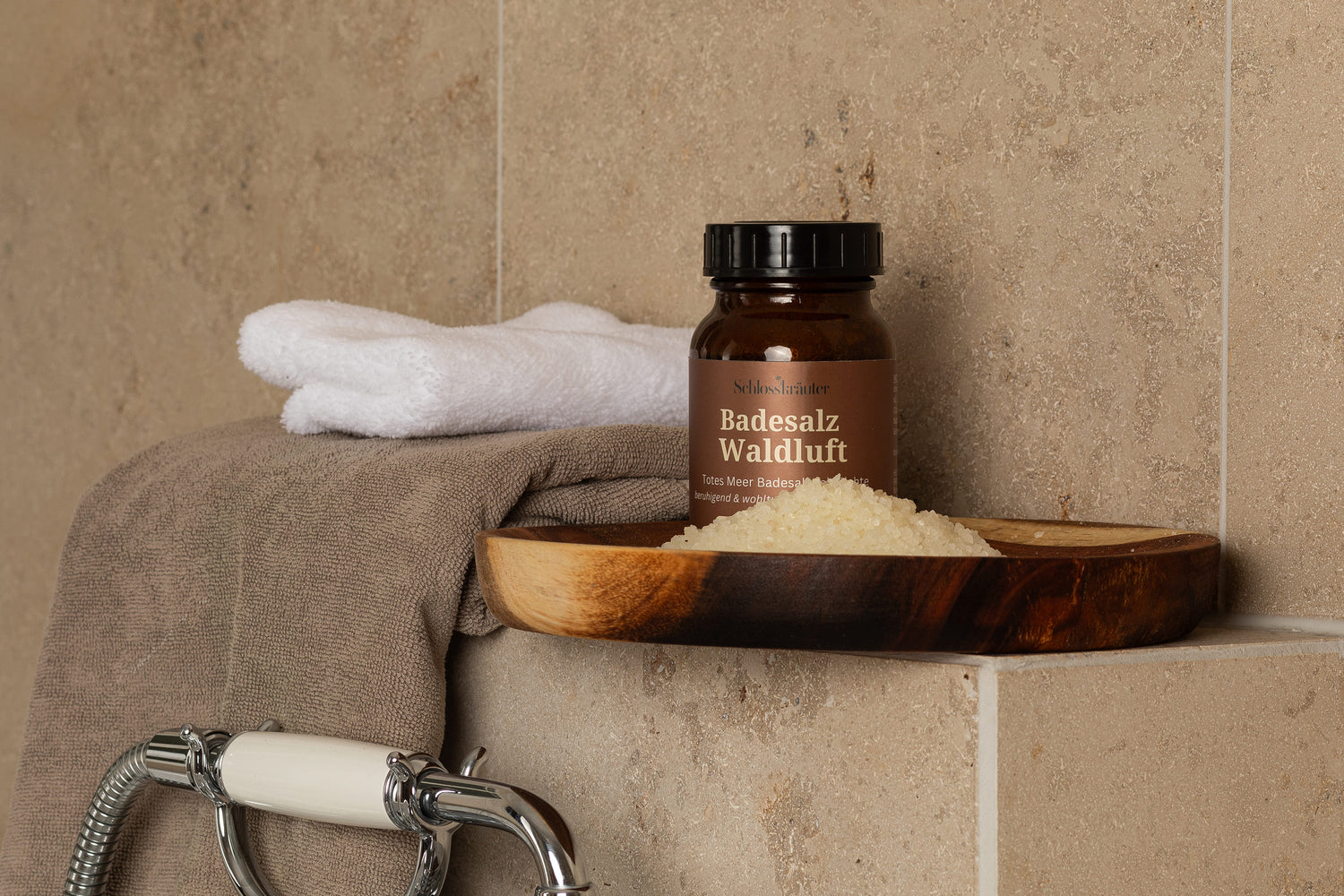 Braune Glasdose mit Totem Meer Erkältungsbad auf einem Holzbrett, das auf Fliesen neben einer Badewanne steht, daneben liegen zwei Handtücher