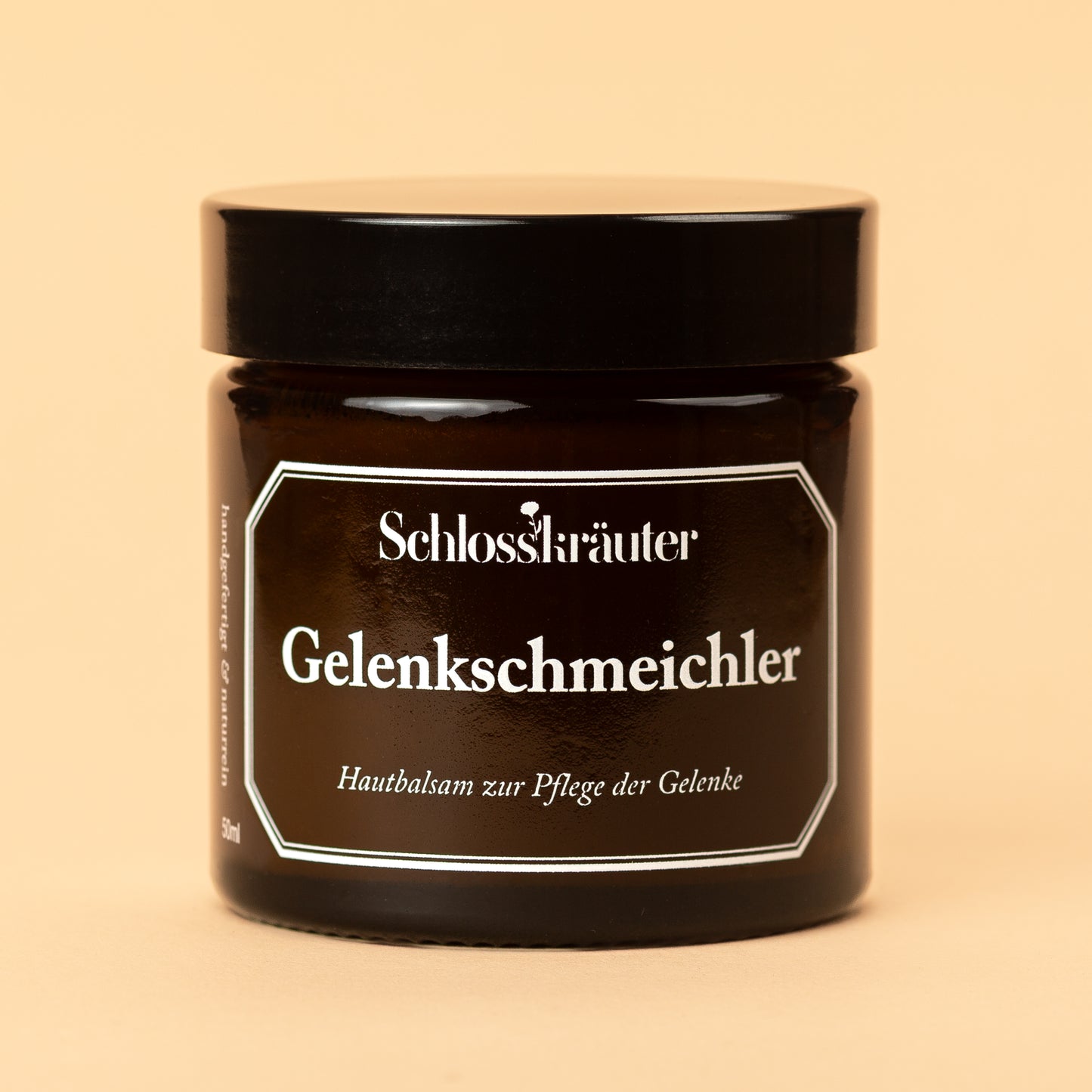 Braunes Glas mit schwarzem Deckel und Etikett „Gelenkschmeichler – zur Pflege der Gelenke“, vor beigem Hintergrund.