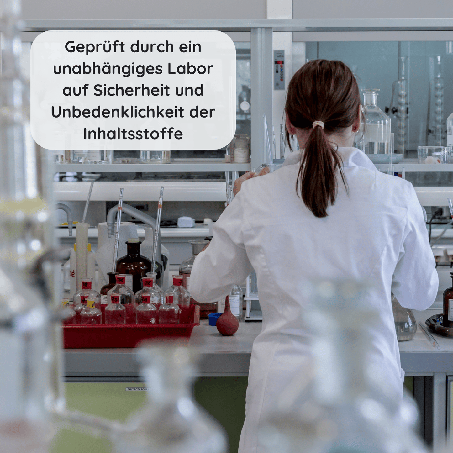 Frau im weißen Laborkittel arbeitet in einem Prüflabor mit Glasgefäßen zur Kontrolle von Inhaltsstoffen mit Text "Geprüft durch ein unabhängiges Labor auf Sicherheit & Unbedenklichkeit der Inhaltsstoffe"