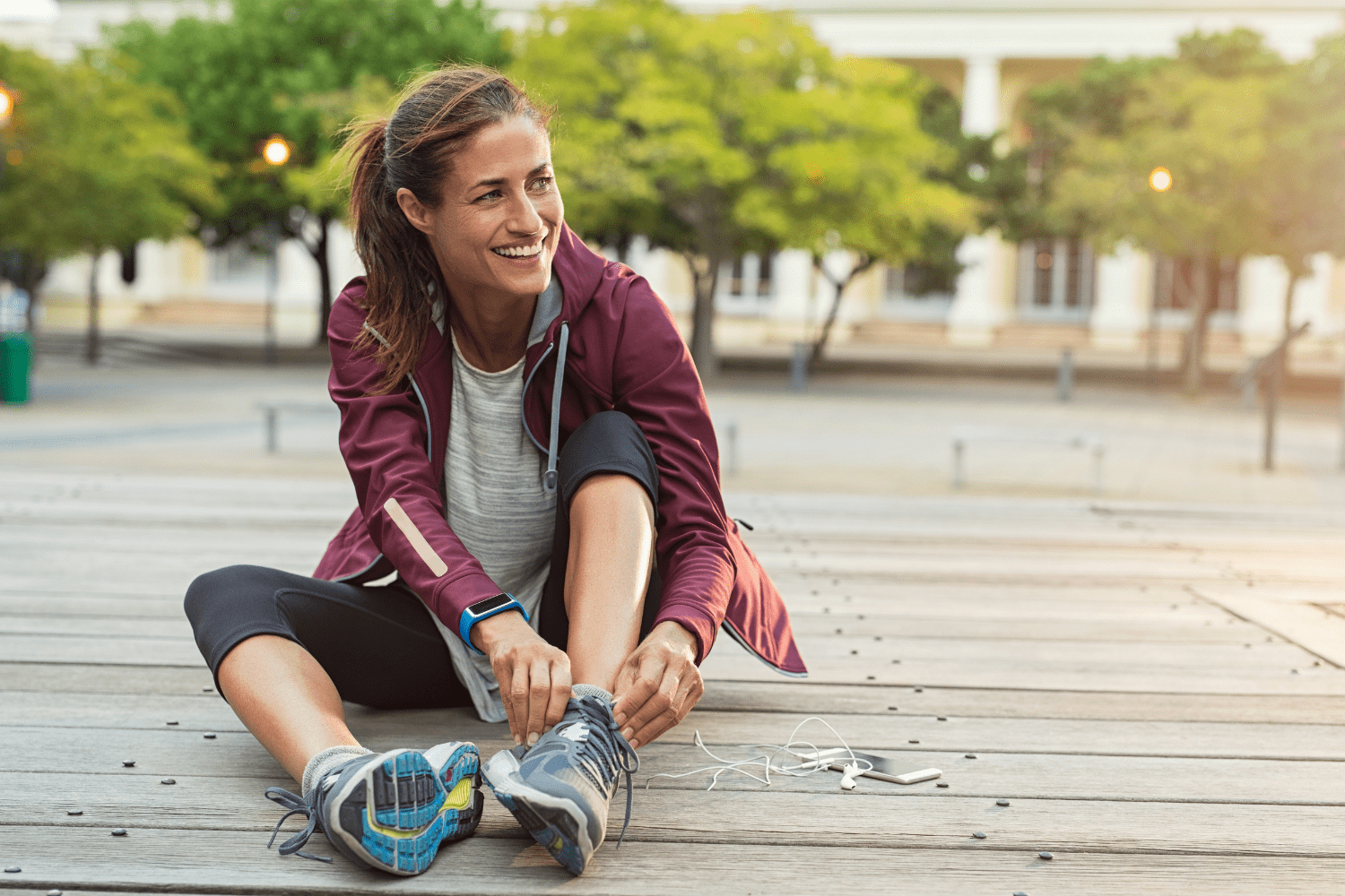 Eine Frau in Sportkleidung sitzt auf einem Holzuntergrund und bindet sich ihre Laufschuhe. Die Fraut sieht aus als würde sie gleich laufen gehen, damit sie entschlacken und den Stoffwechsel beschleunigen kann