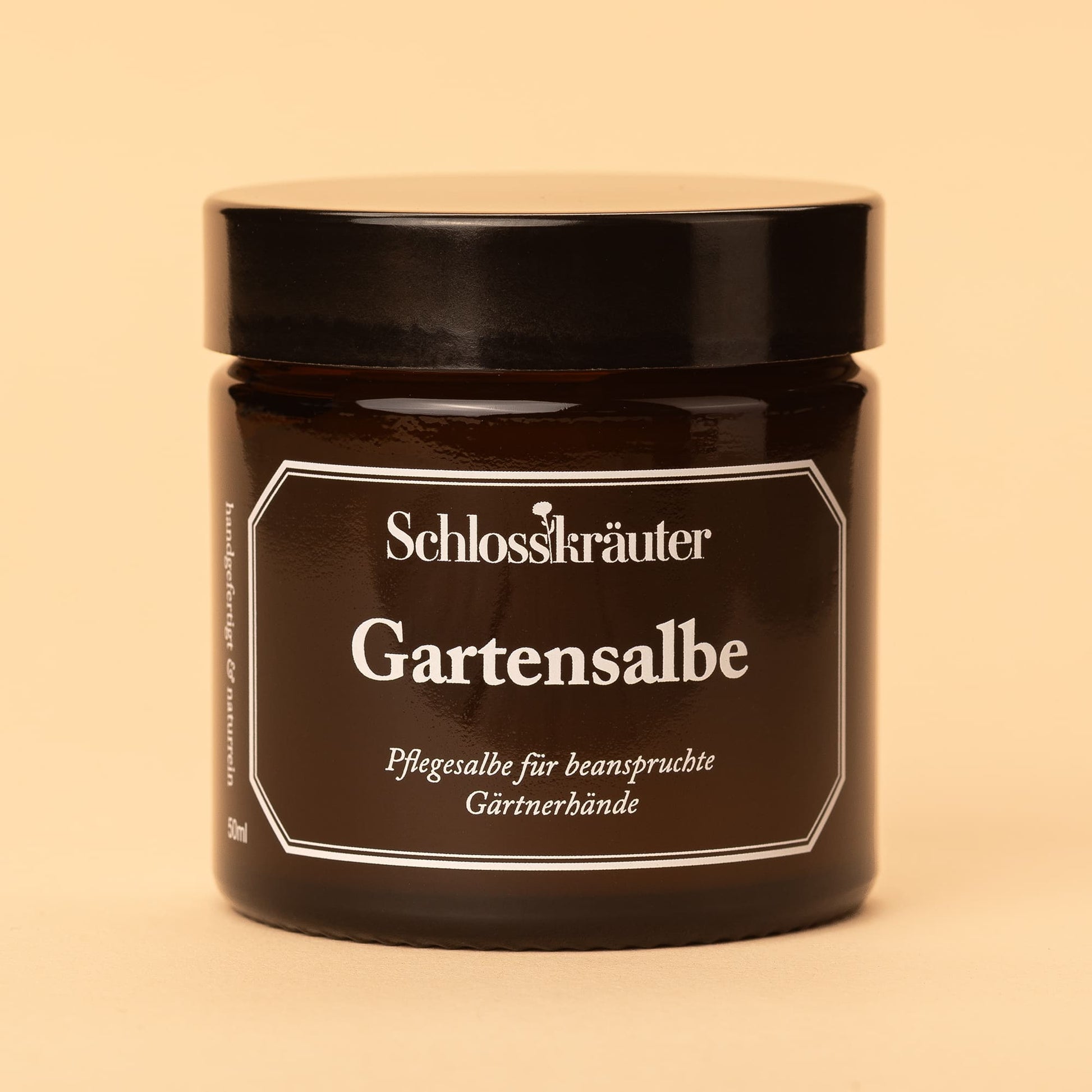 Braunes Glas mit geschlossenem Deckel und dem Etikett „Gartensalbe – Pflegesalbe für beanspruchte Gärtnerhände“, vor hellem Hintergrund.