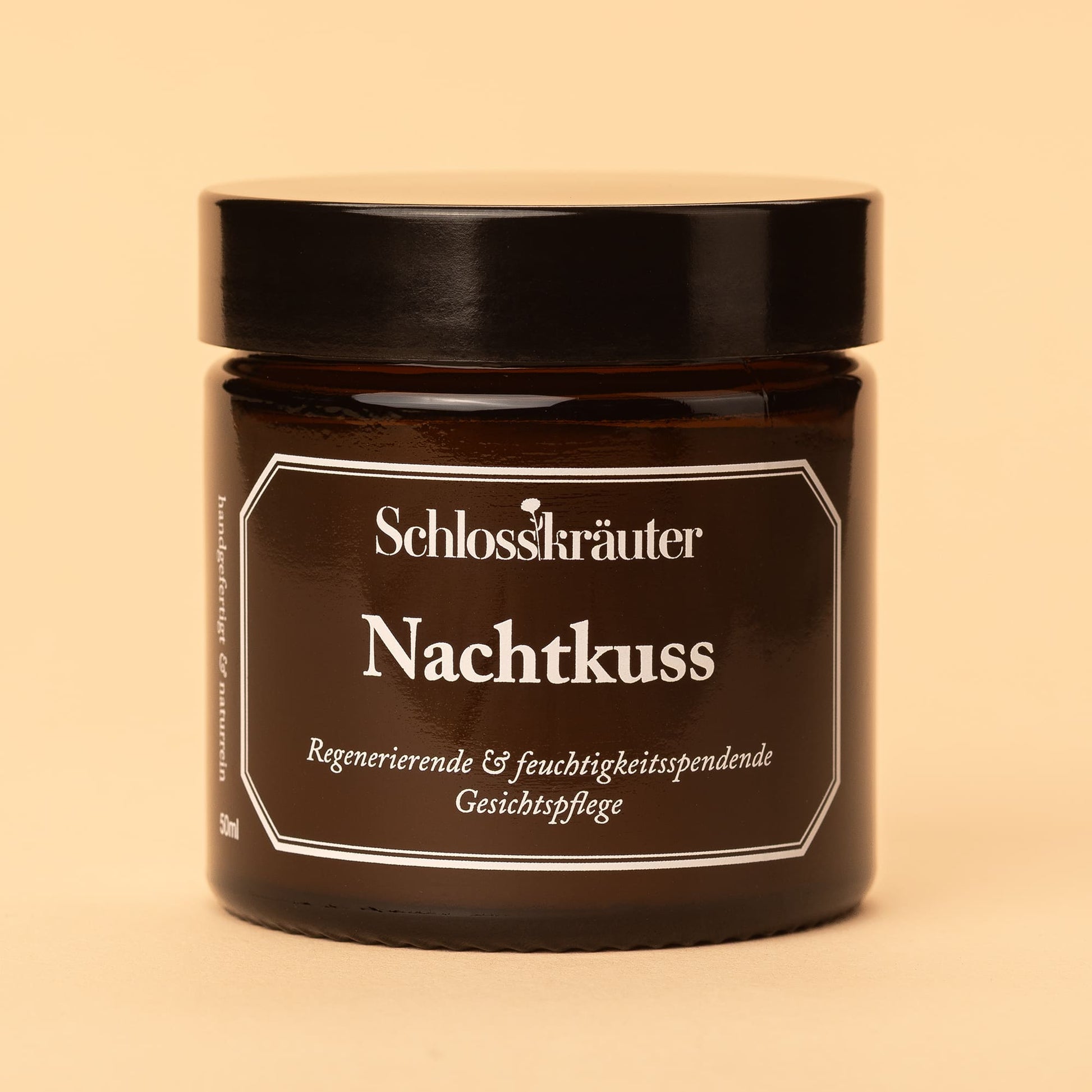 Braunes Glas mit schwarzem Deckel und Etikett „Nachtkuss – regenerierende und feuchtigkeitsspendende Gesichtspflege“, vor hellem Hintergrund.