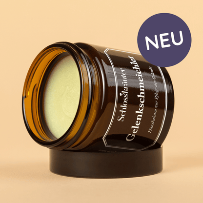 Braunes Glas mit grünlicher Salbe für die Hautpflege bei Gelenkbeschwerden auf beigem Hintergrund mit Auschrift "NEU"