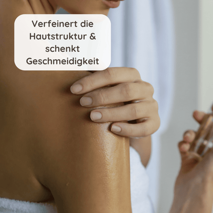 Frau trägt Körperöl auf die Schulter auf, die Haut glänzt leicht, Fokus auf sanfte Hautpflege.