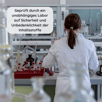 Frau im weißen Laborkittel arbeitet in einem Prüflabor mit Glasgefäßen zur Kontrolle von Inhaltsstoffen mit Text "Geprüft durch ein unabhängiges Labor auf Sicherheit & Unbedenklichkeit der Inhaltsstoffe"