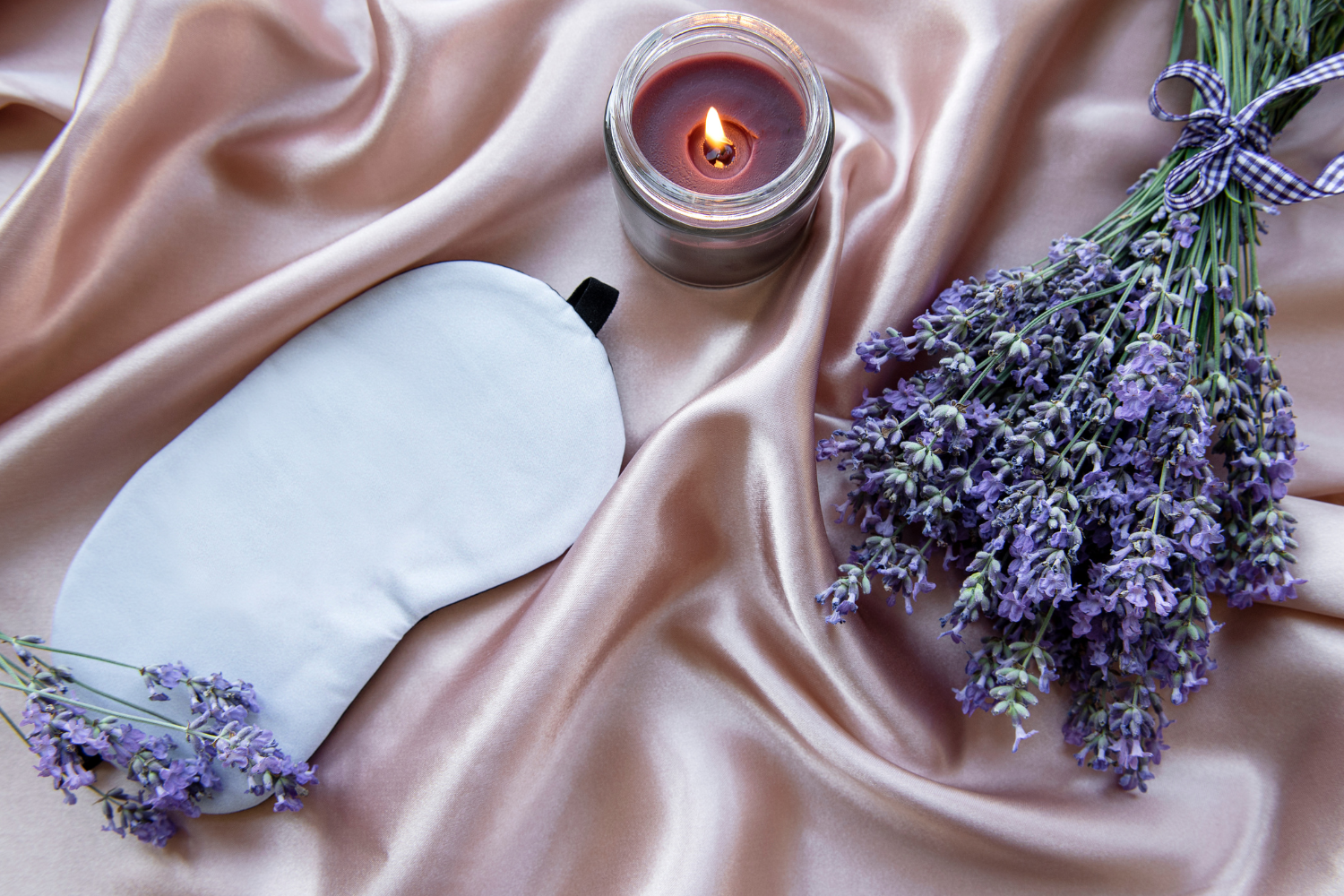 Getrockneter Lavendel, Schlafmaske und Kerze auf einer pinken Bettdecke